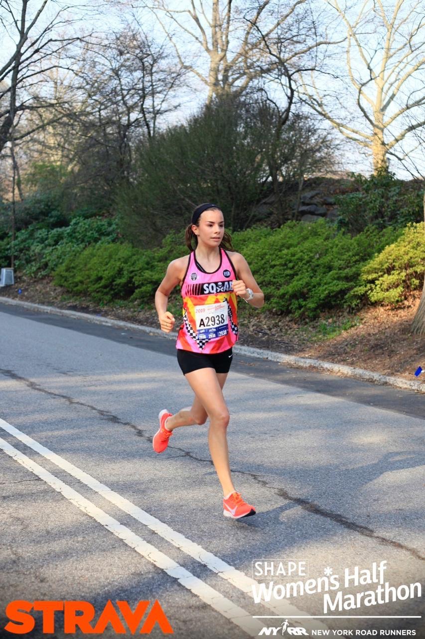Fátima Alanís racing the SHAPE Women's Half Marathon in Central Park, New York, with NYRR signage in view.